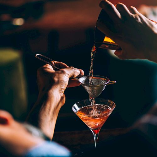A close-up of a person wearing a hood and sunglasses, holding a cigarette; dark, moody lighting, urban vibe.
