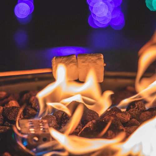 A bonfire with flames and glowing logs, set indoors with colorful lights in the background.