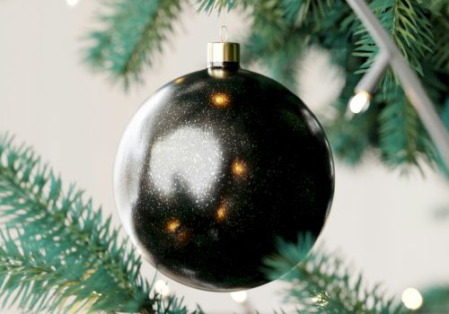 A close-up of a Christmas tree with a shiny black ornament and string lights.