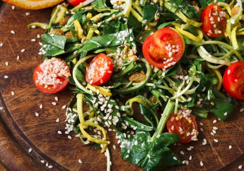 Fresh greens, cherry tomatoes, and spiralized zucchini noodles tossed with sesame seeds and herbs on a wooden plate. End.