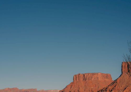 A tranquil desert river winds through red rock formations under a clear blue sky, reflecting the landscape in its calm waters.