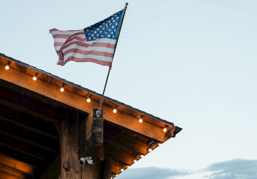 An American flag on a pole above a wooden porch with string lights, set against a canyon backdrop.